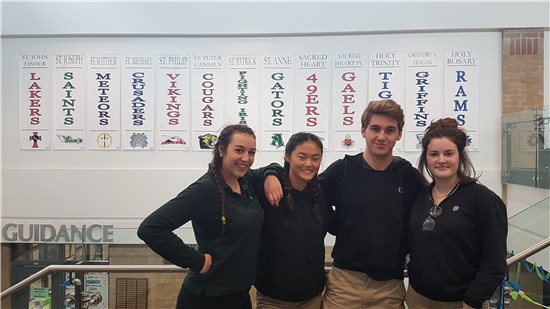 Four smiling students stand in St. Patrick's Catholic High School in front of the elementary feeder schools' banners.